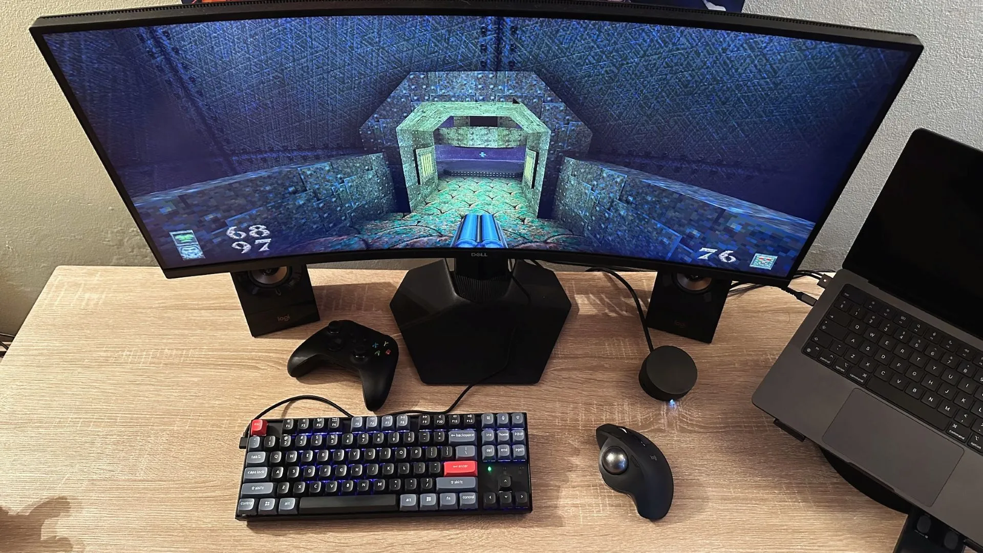 Bàn làm việc với TV làm màn hình, hình ảnh game Quake hiển thị cùng trackball Logitech trên bàn